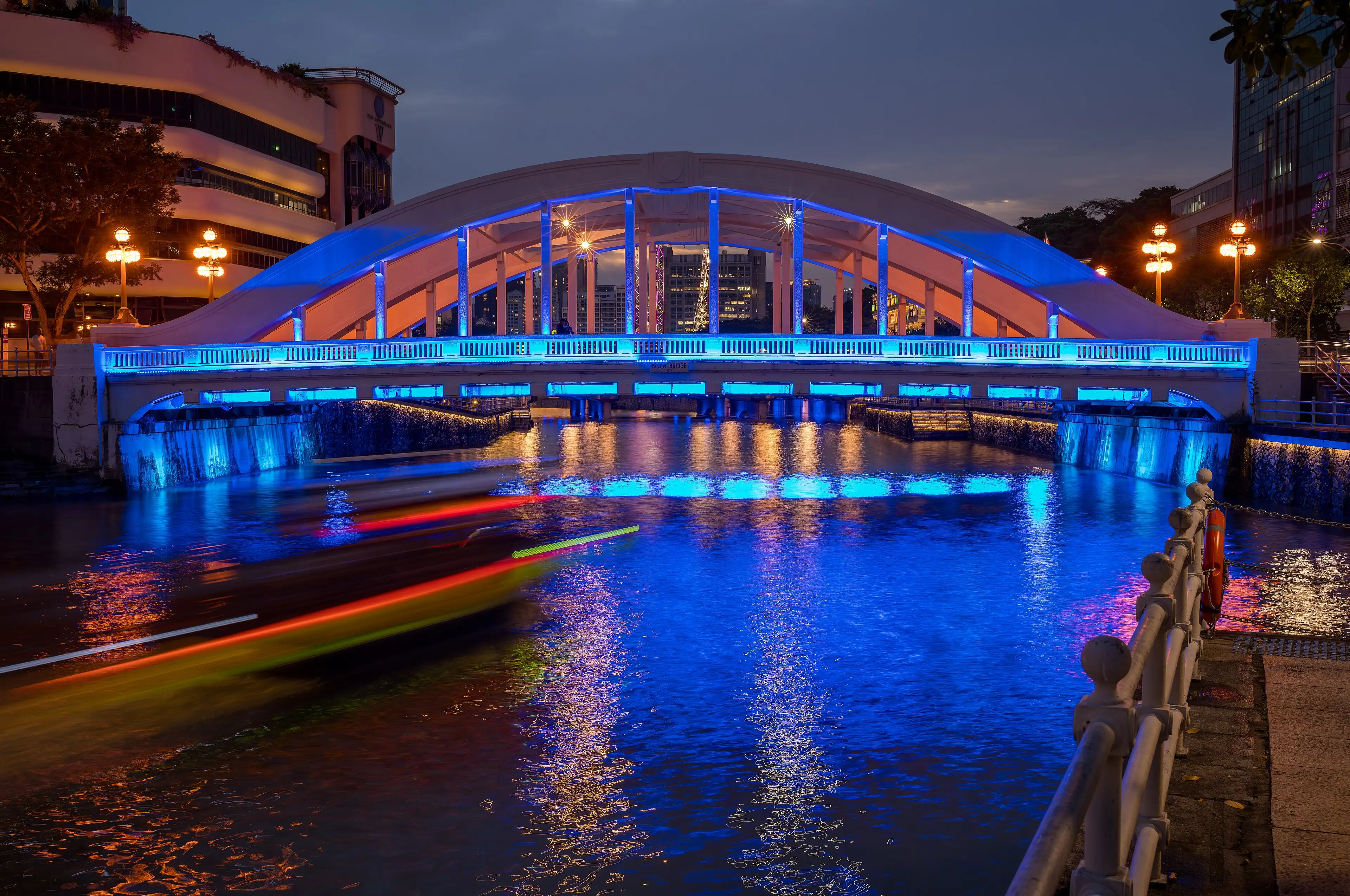 The Elgin Bridge lit blue at dusk, with a boat passing underneath.