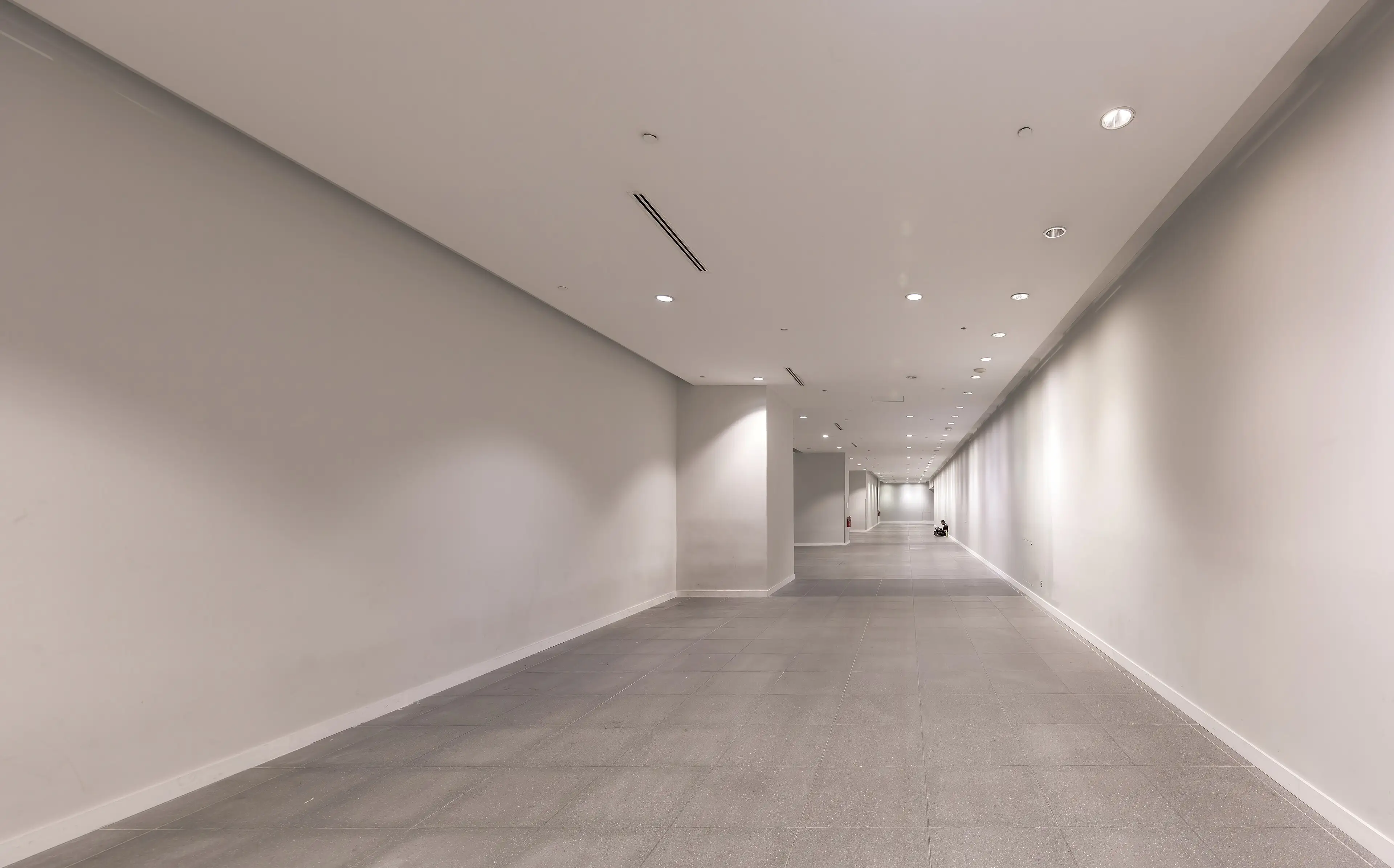 An empty white corridor in Marina Bay MRT station, with one person sitting far away.